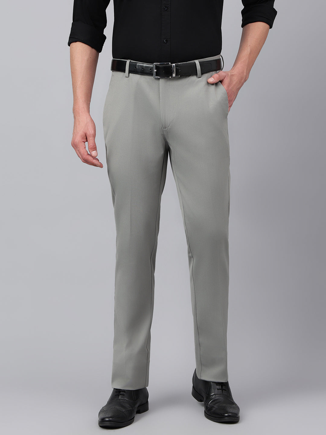 A man standing, wearing grey standard fit solid formal trousers with a black belt, a white shirt, and black shoes.