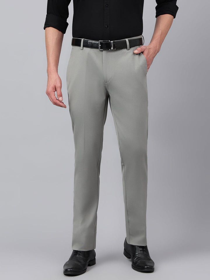 A man standing, wearing grey standard fit solid formal trousers with a black belt, a white shirt, and black shoes.