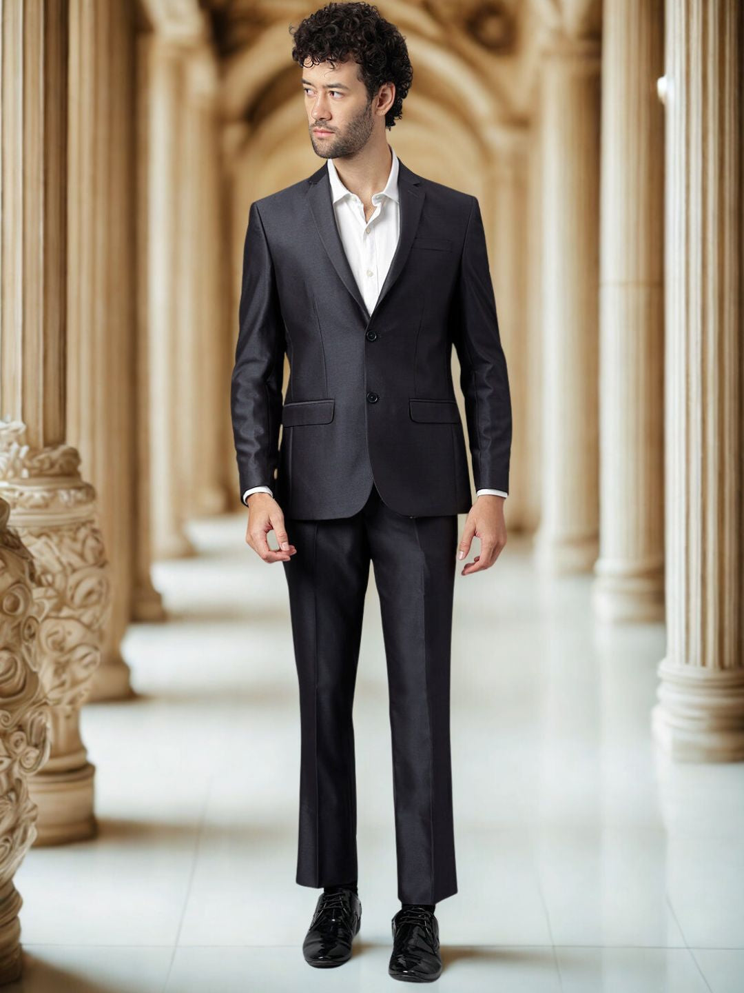 Man wearing a black suit standing in an elegant hallway with columns.