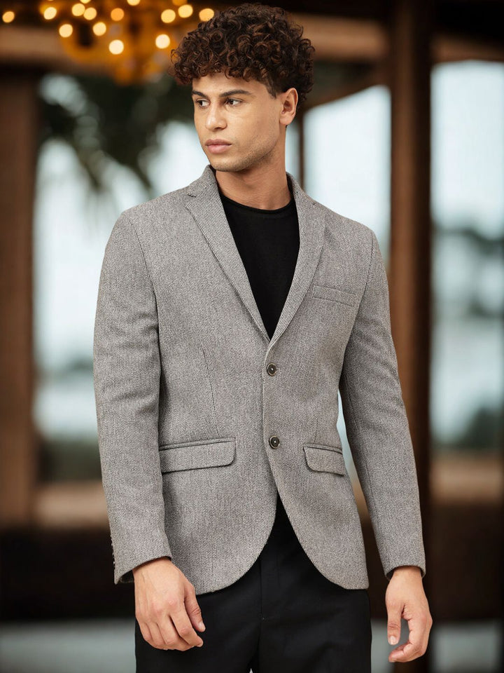 Man wearing a gray blazer over a black shirt with a blurred background