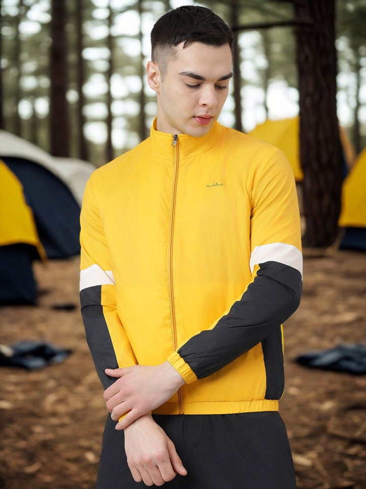 Person wearing a yellow jacket with black sleeves in a forest setting with tents.