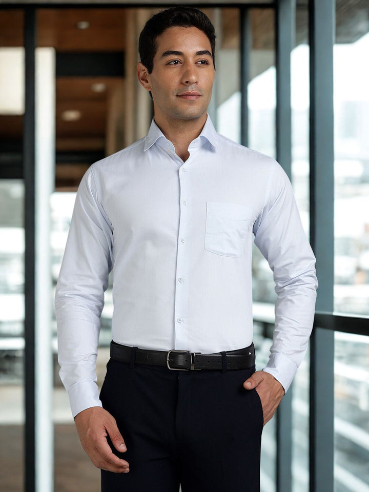 Man wearing a light blue dress shirt and black pants standing indoors.