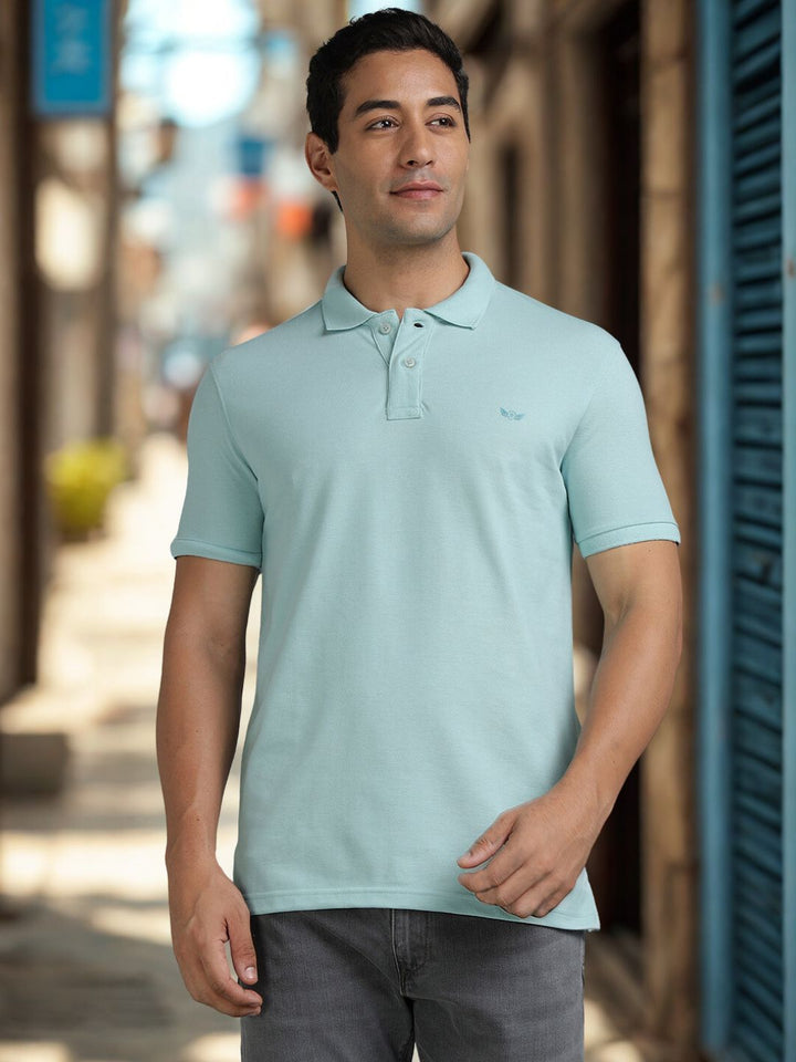 Man wearing a light blue polo shirt standing on a street.