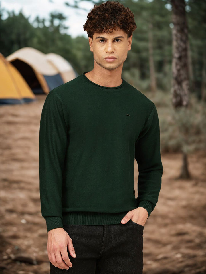 Man wearing a green sweater standing in a forest with camping tents in the background