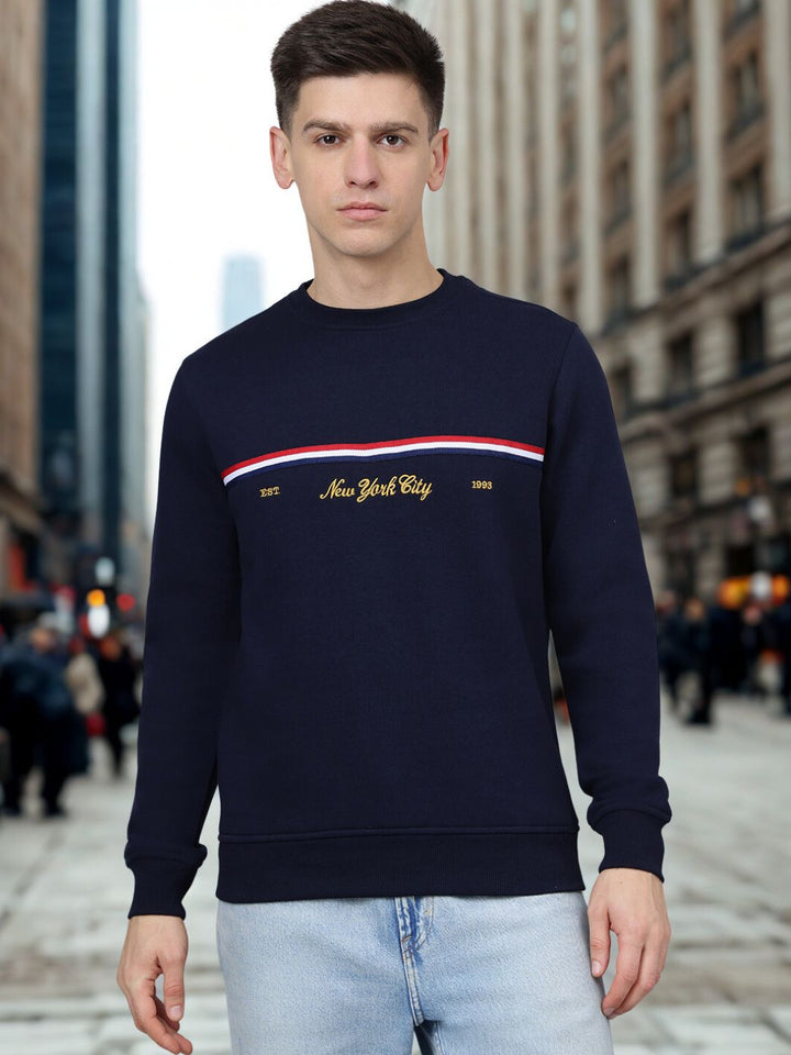 Person wearing a navy blue sweatshirt with 'New York City' text and red and white stripe, standing on a city street.