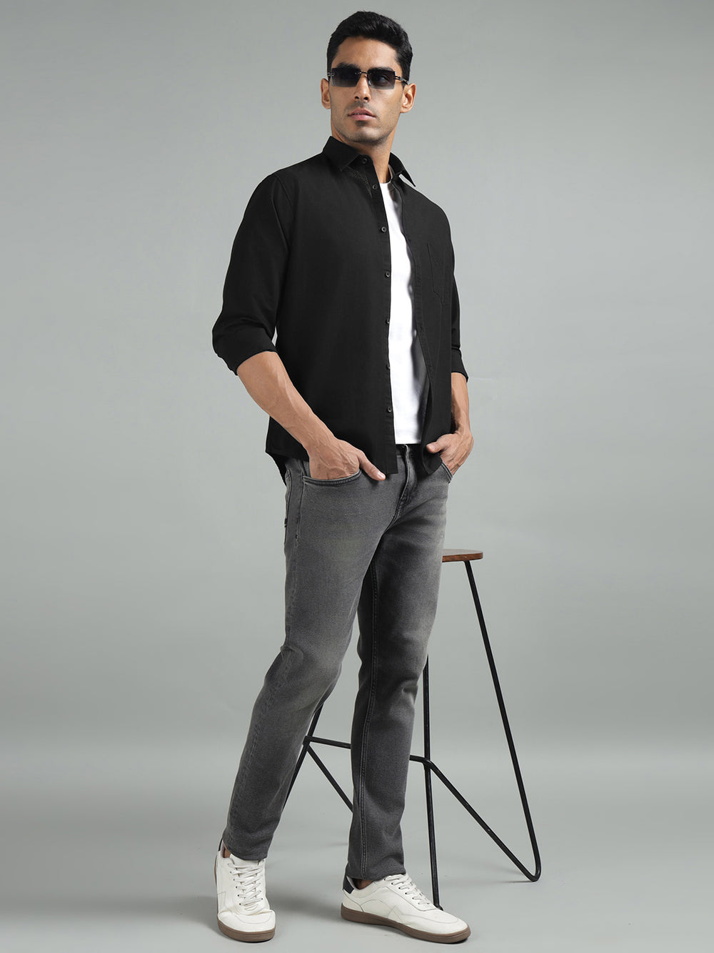 Man in black shirt and gray pants standing on a stool against a gray background