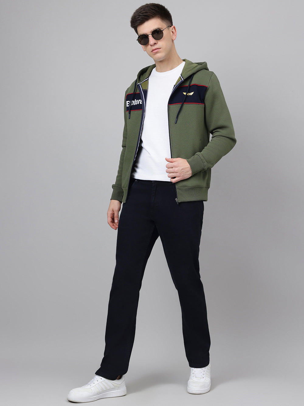 Man wearing a green hoodie with a brand logo, black pants, and white sneakers on a gray background