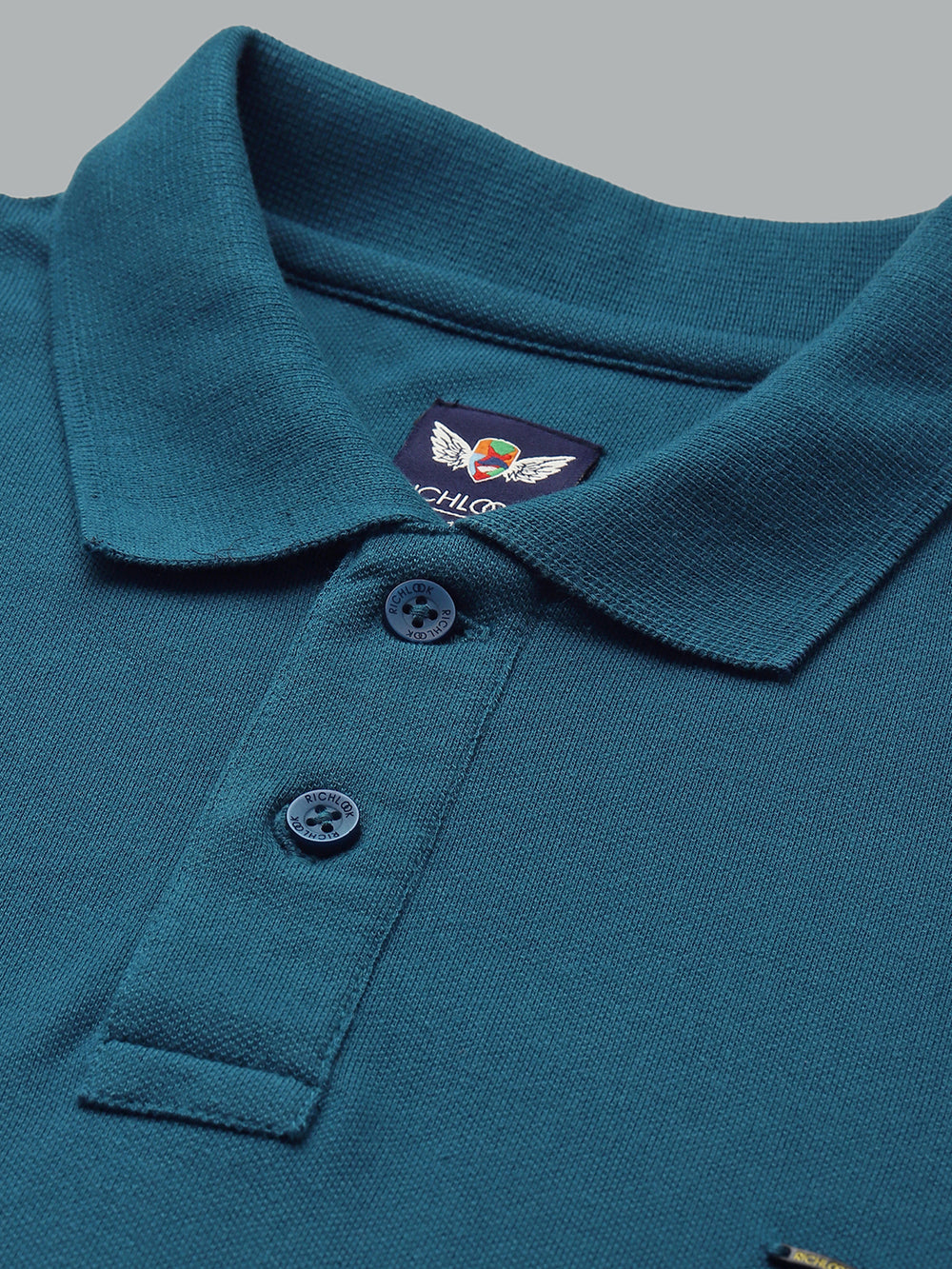 Close-up of a teal polo shirt with a brand logo on a gray background