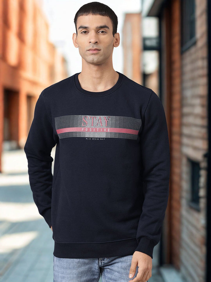Man wearing a black sweatshirt with a graphic design standing in an urban setting.