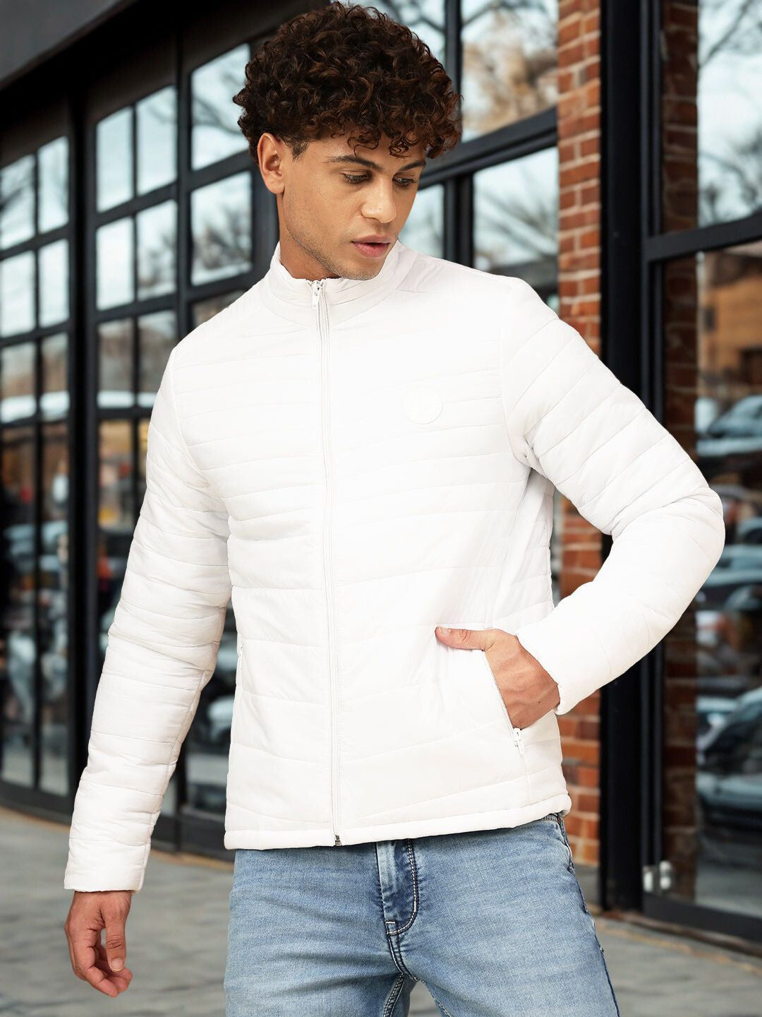 Man wearing a white puffer jacket and light blue jeans standing outdoors.